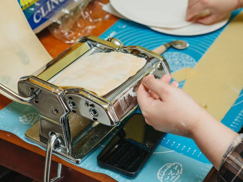 Hands rolling pasta dough in machine
